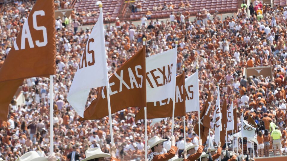 The University of Texas marching band members hold orange and white flags that say "Texas"
