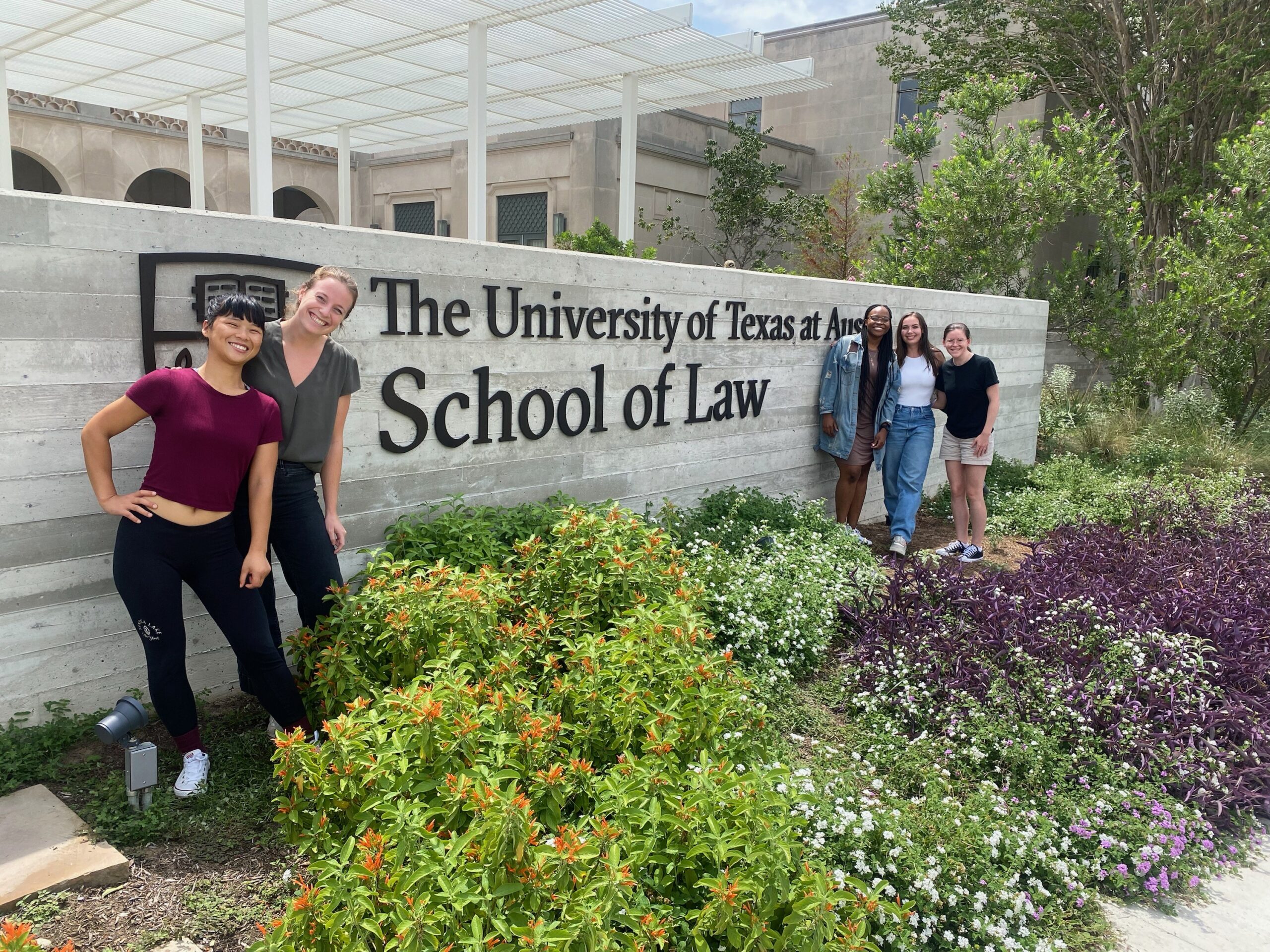 Five women stand in front of a low brick wall with The University of Texas School of Law work mark on its facade