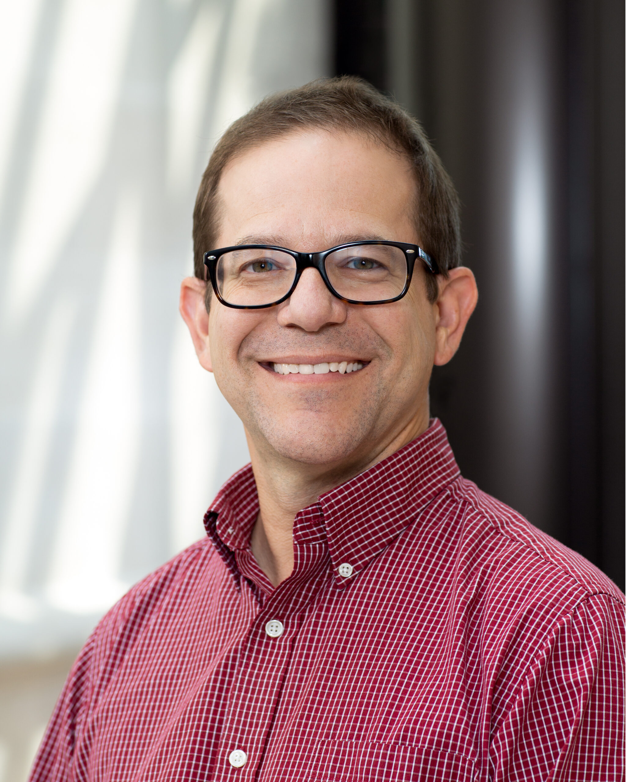 Portrait of Michael Harvey wearing an read and white checkered button-down shirt.