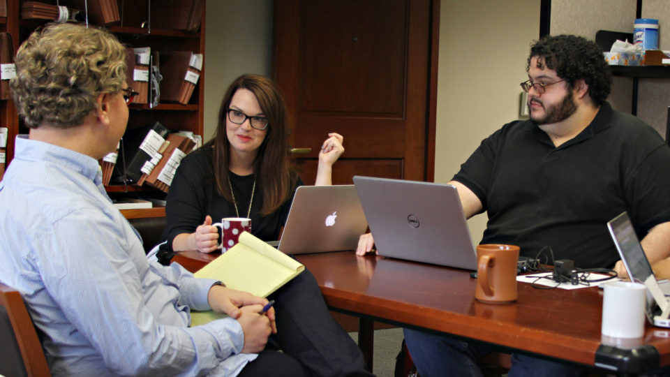 Faculty members sit at a table with laptops