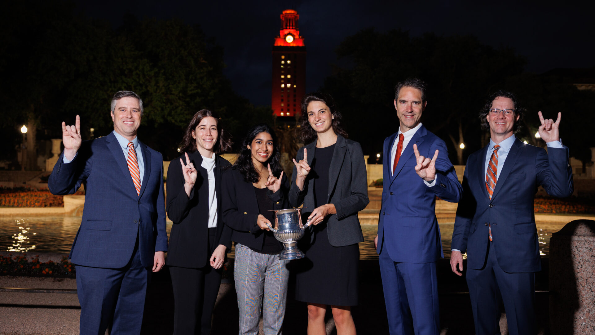 Students and faculty standing in front of the University of Texas Tower holding a trophy.