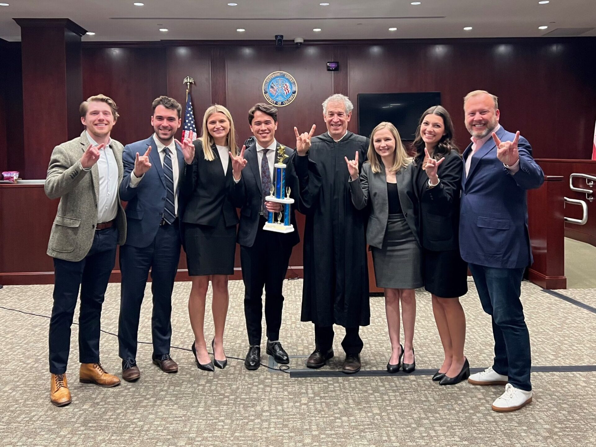 Mock trial team of students and coaches holding trophy, standing in courtroom 
