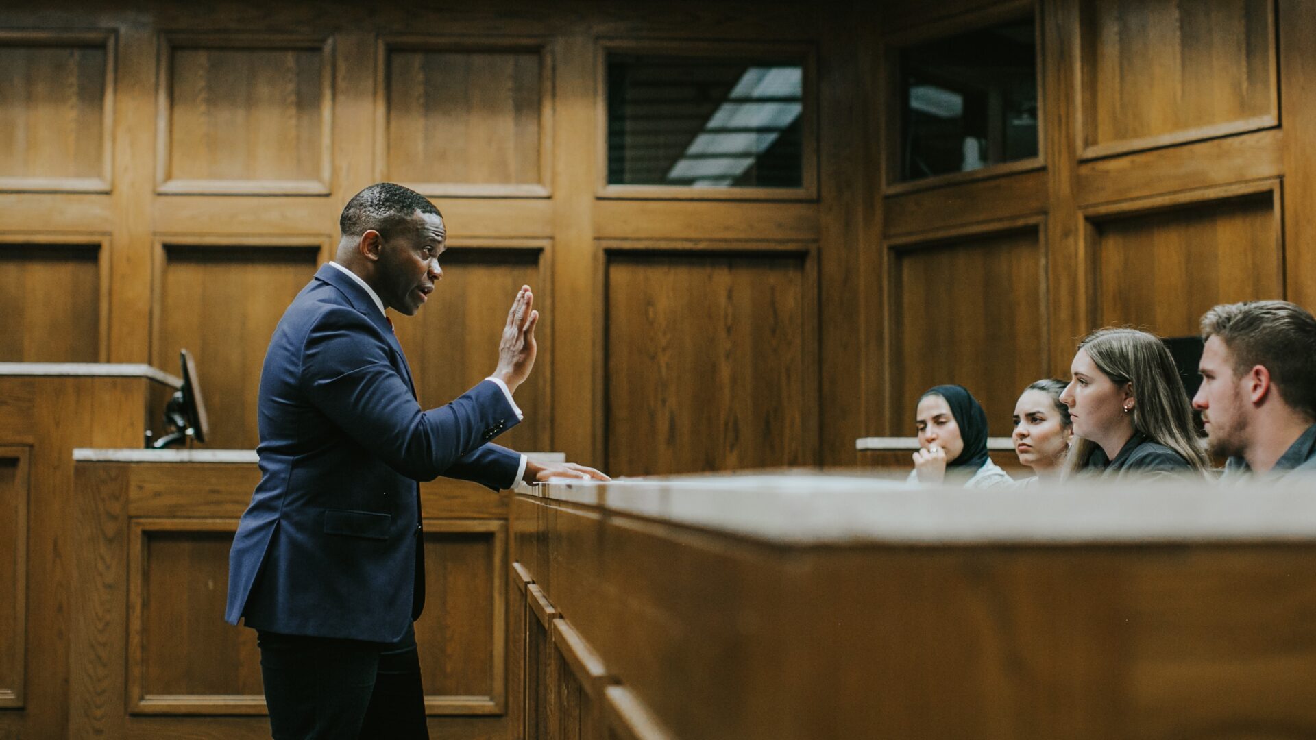 Adjunct professor teaching class to students seated in the jury box of a courtroom
