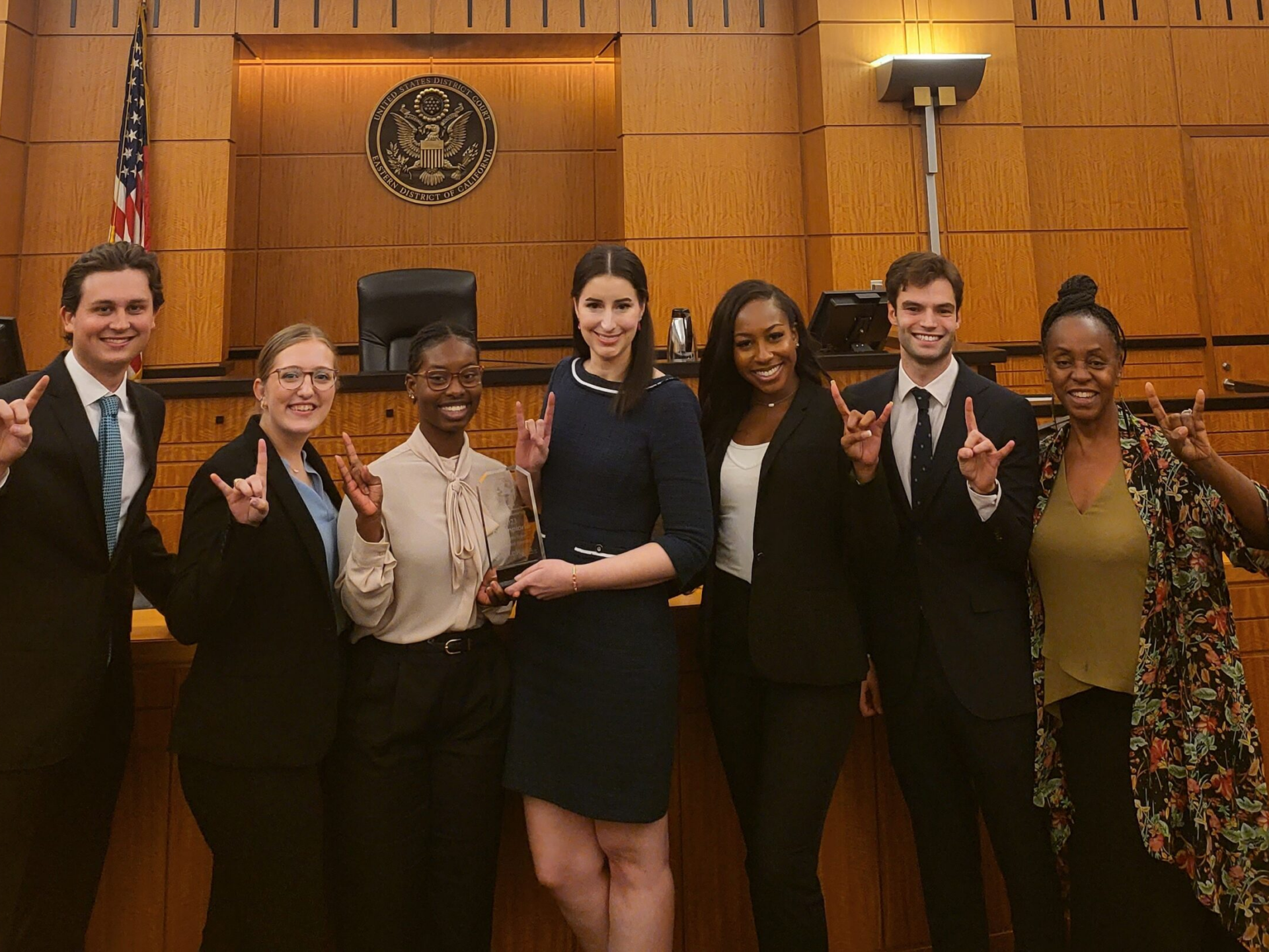 group standing in front of courtroom holding trophy and showing hook ’em hand signs