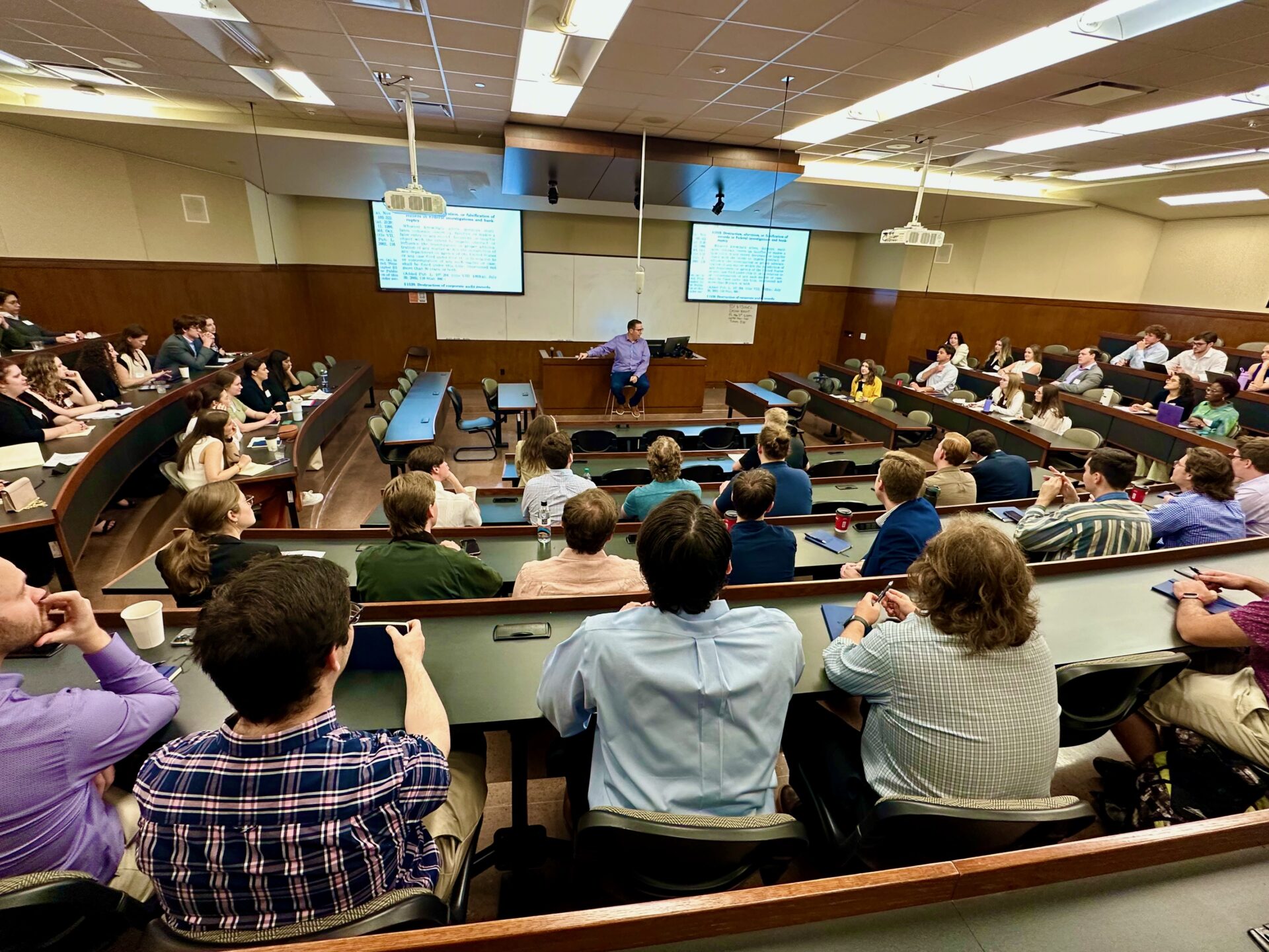 A law professor sits at the front of a full lecture classroom