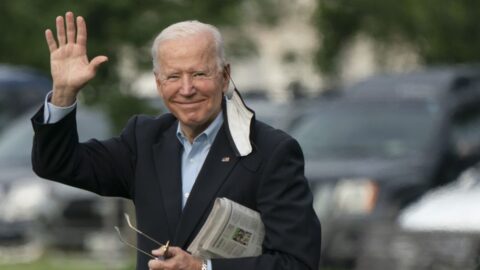 President Biden holding a newspaper in his left hand, while waving with his right hand