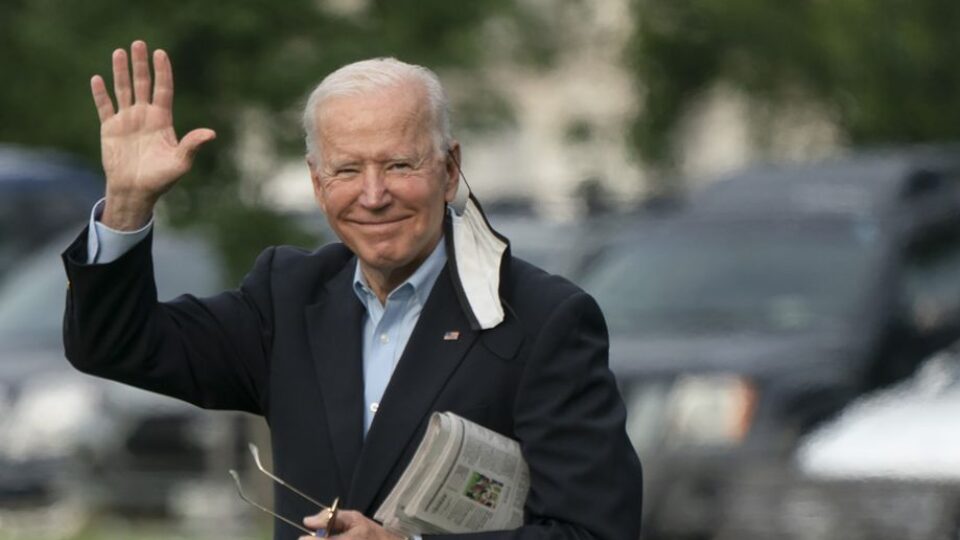 President Biden holding a newspaper in his left hand, while waving with his right hand