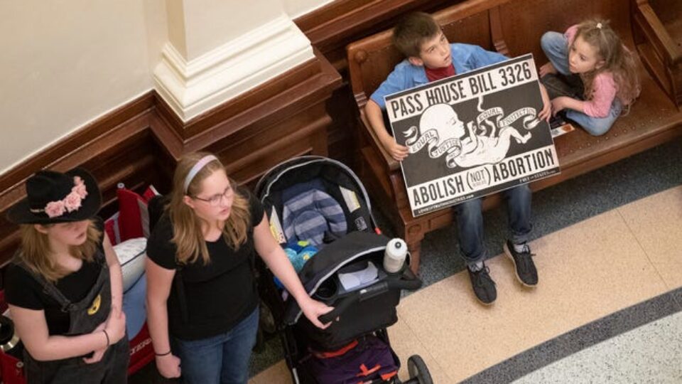 Anti-abortion advocates in a building, with a young boy holding a poster of a fetus.