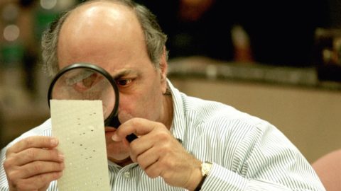 A man using a magnifying glass to read a ballot from the 2020 Presidential election.