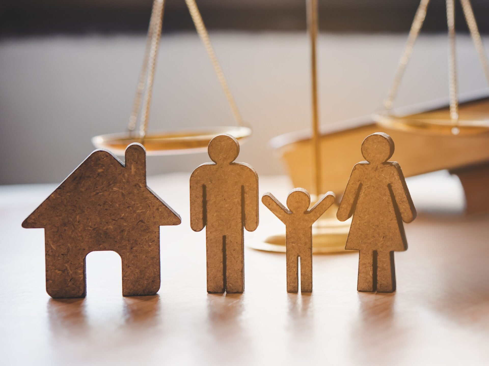 wood cutouts of house and family in front of scales of justice