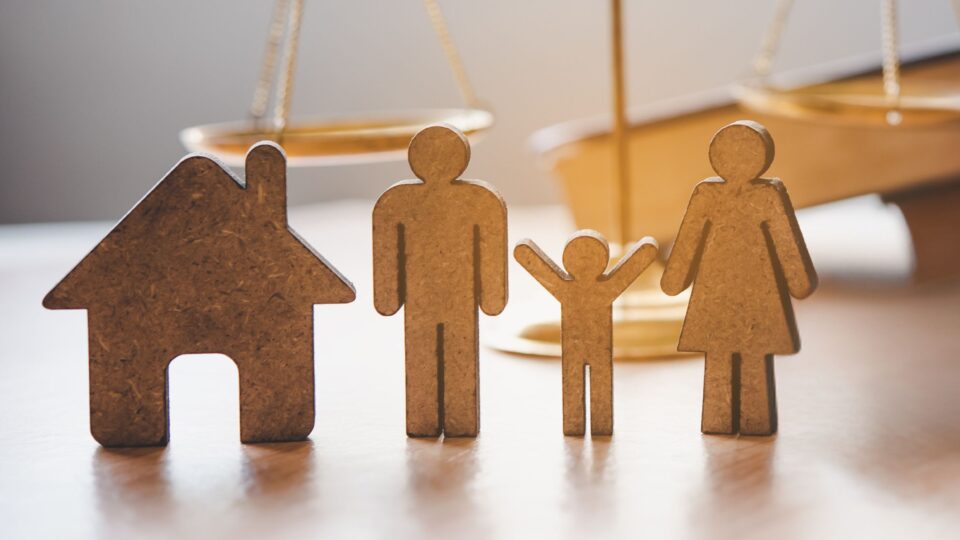 wood cutouts of house and family in front of scales of justice