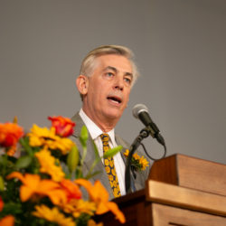 Neal Manne, speaking into a microphone in front of a podium.