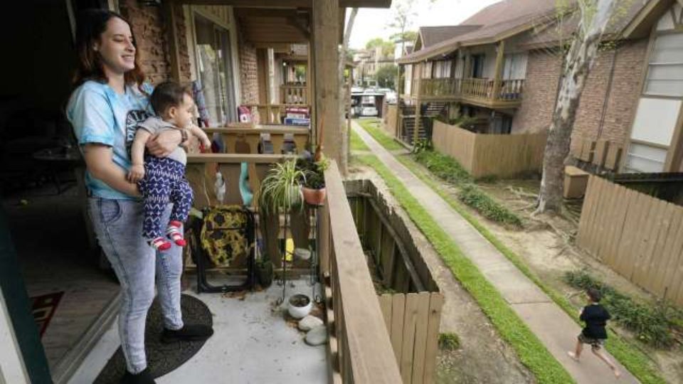 A woman holds an infant while standing on an apartment balcony