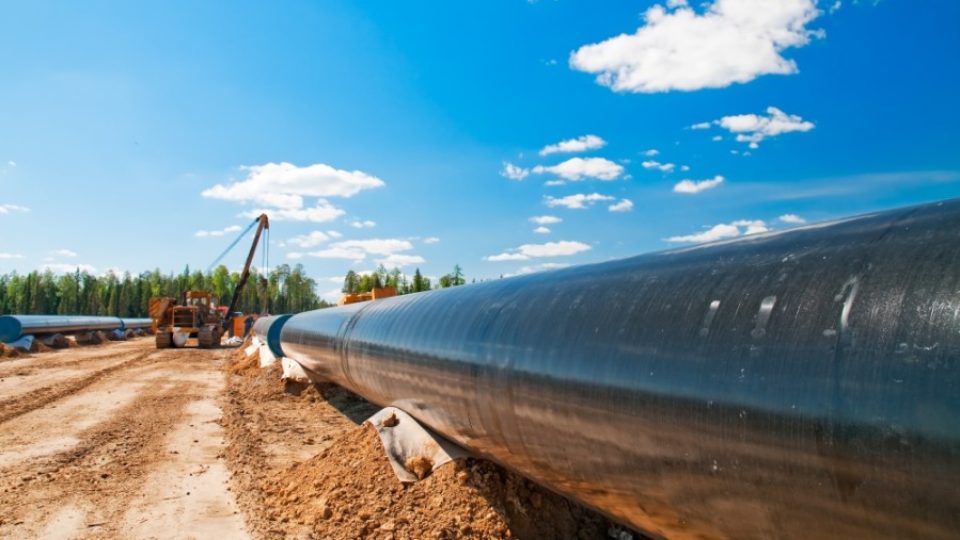 A gas pipeline runs across bare dirt beneath a blue sky