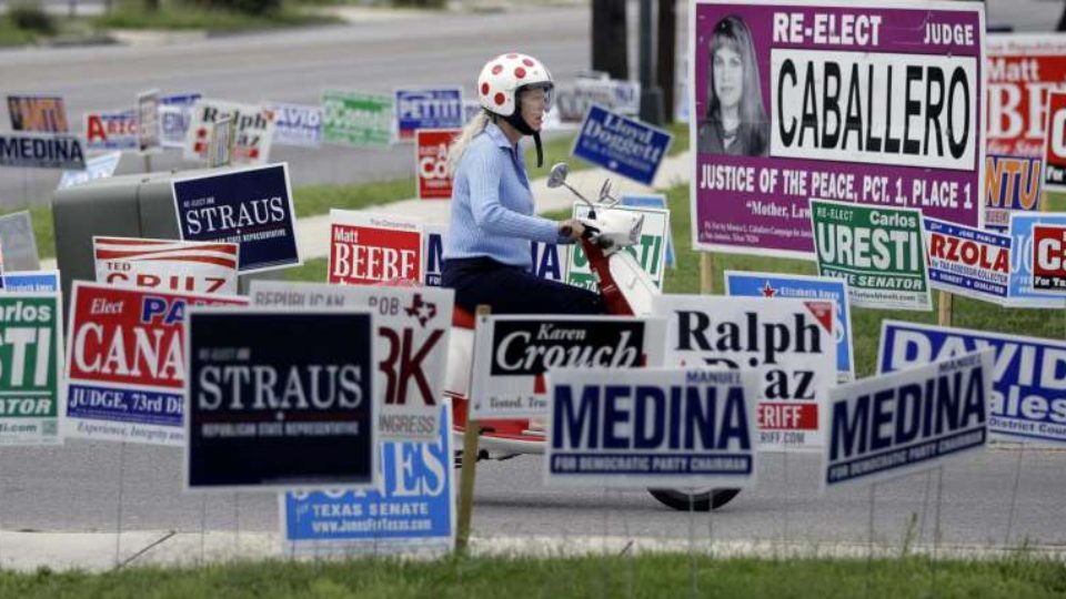 Woman drives a motor scooter past dozens of campaign signs