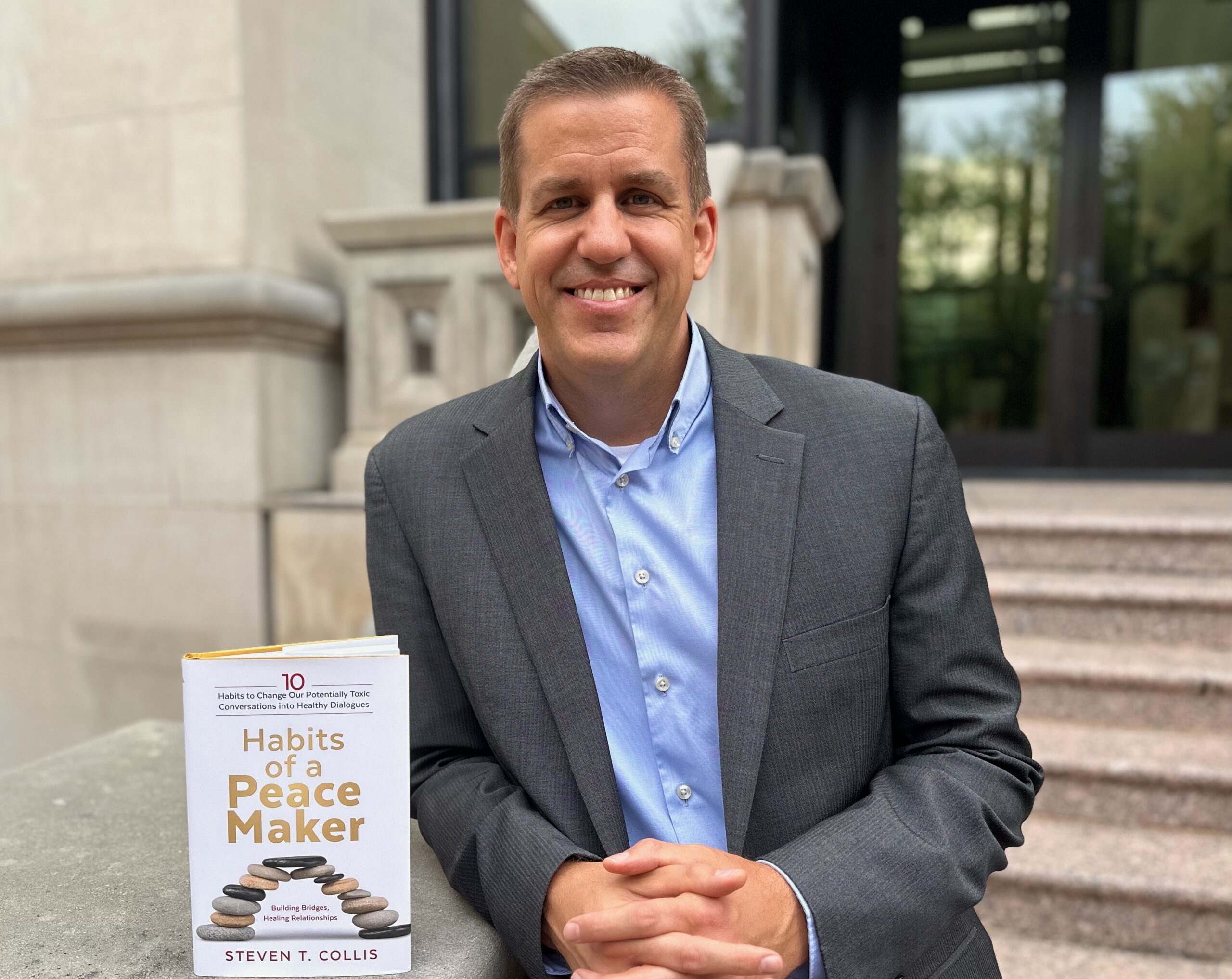 Prof. Steve Collis stands outside the law school with a copy on his new book, 10 Habits of a Peacemaker.