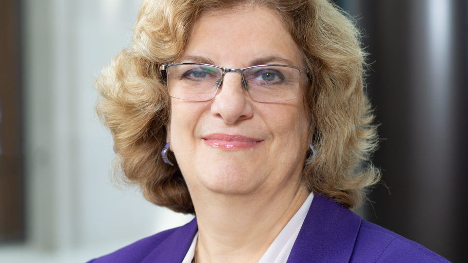 Portrait of Professor Deitch, wearing a purple jacket and blue necklace