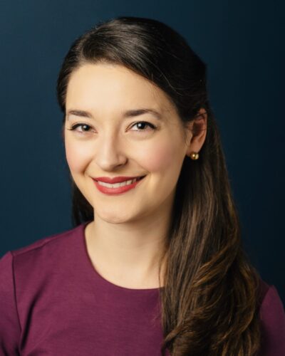 Portrait of Julia Di Fiore, wearing a magenta shirt in front of a dark blue background.