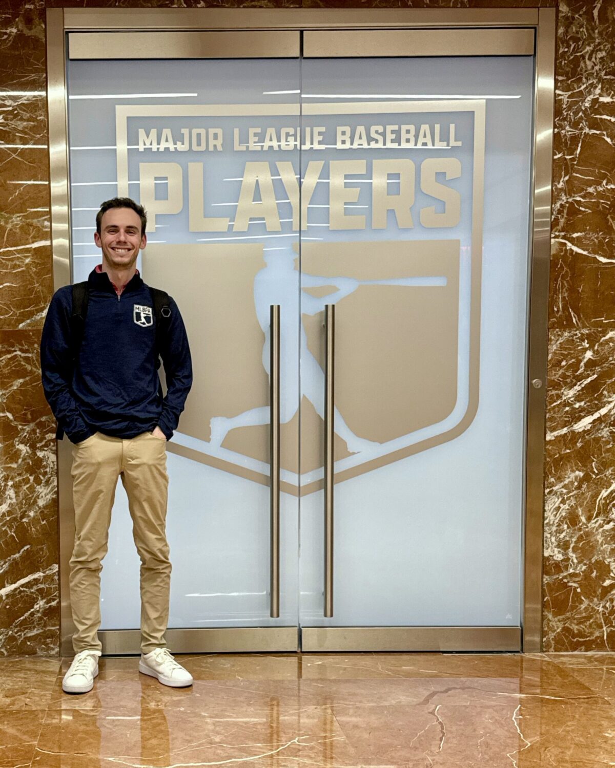 Ryan Faulkner stands in front of a door with the Major League Baseball Players logo.