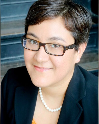 A portrait of Frances Valdez, in a black blazer and pearl necklace and glasses, the executive director of Houston in Action.