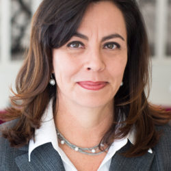 Portrait of Hilda Galvan, wearing a grey suit jacket and a necklace with pearls.