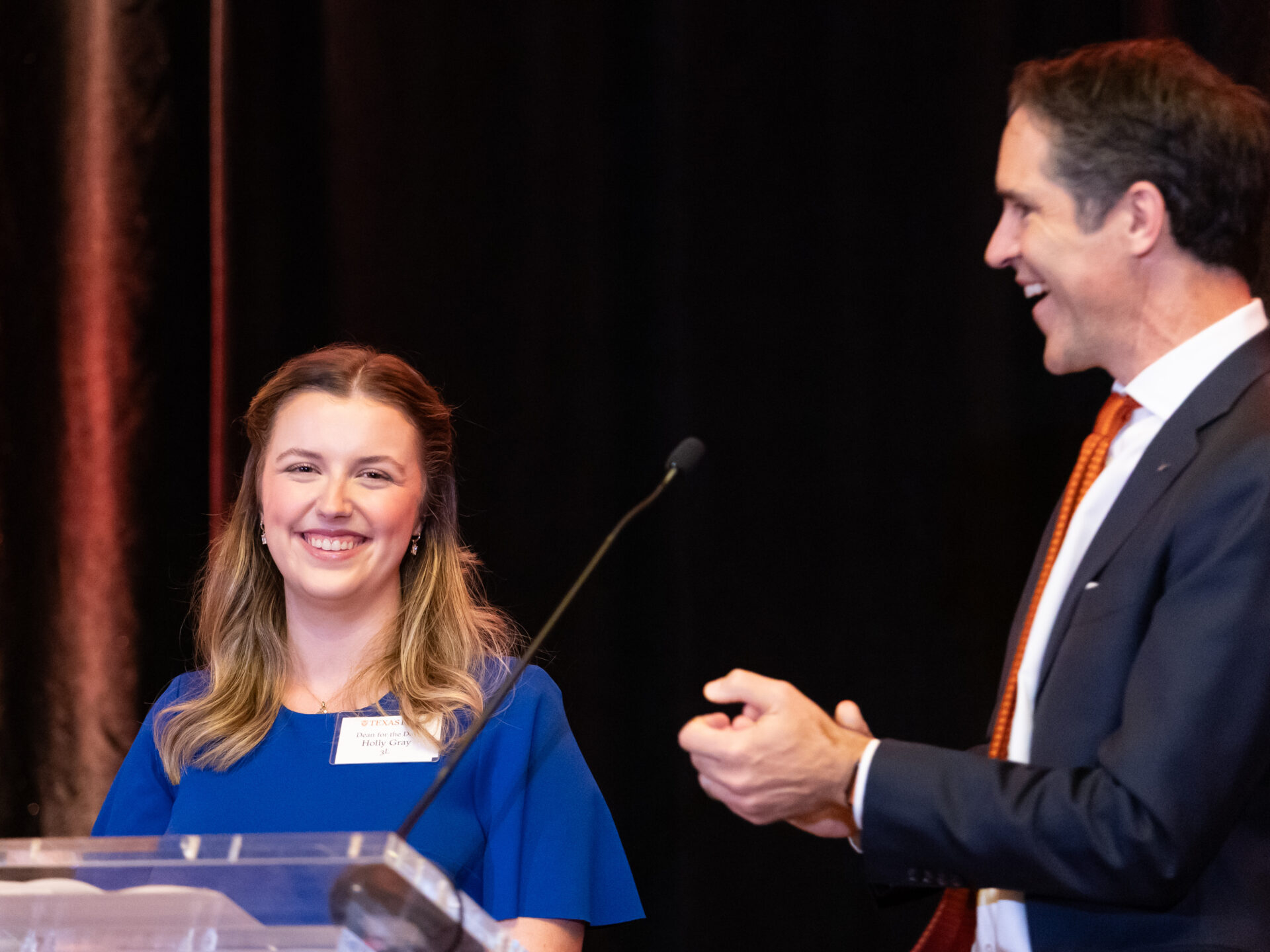 Holly Gray ’26 speaks onstage at the 2025 Alumni Awards and is applauded by Dean Bobby Chesney.