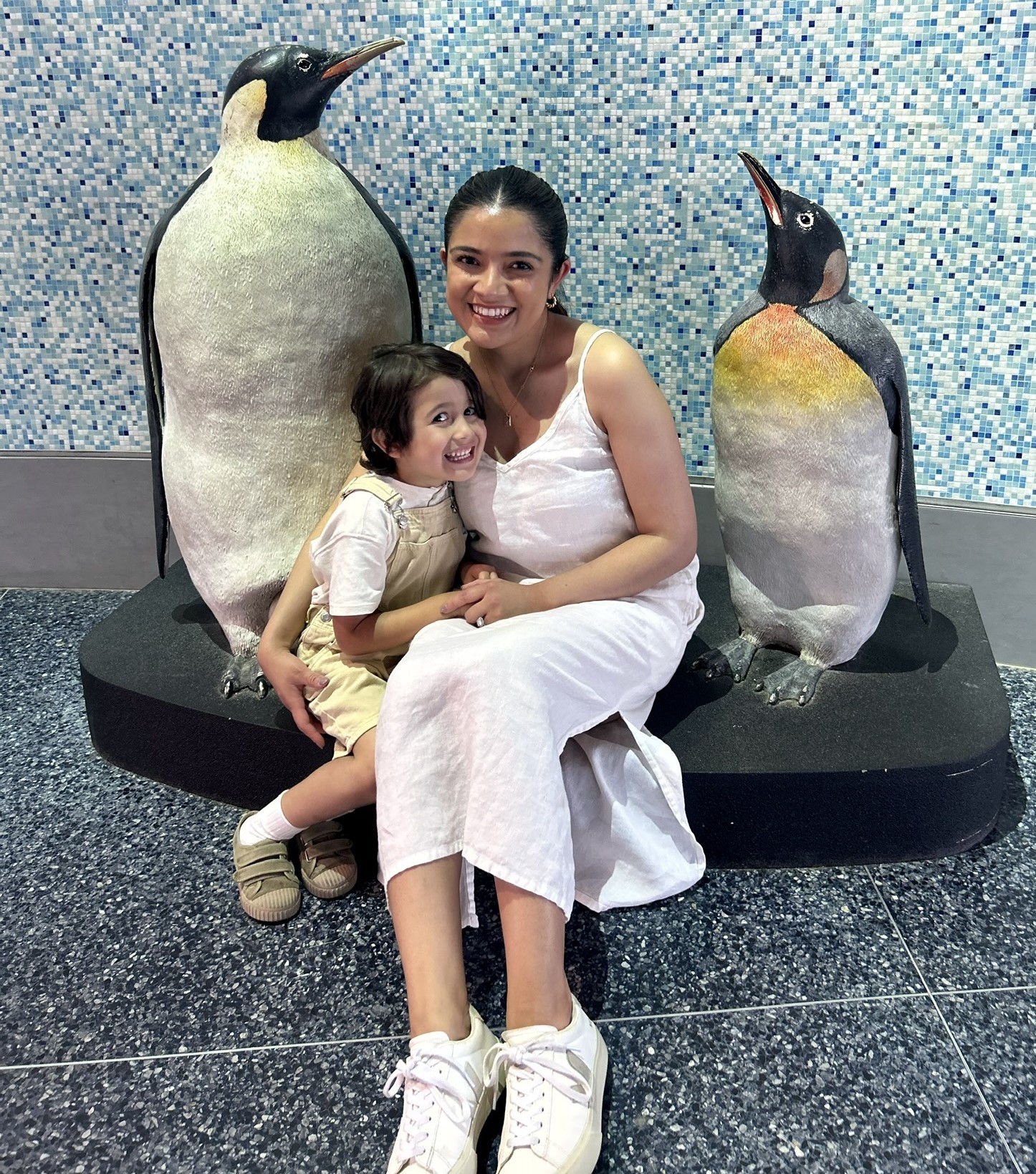 Lizeth sits at an aquarium with her son and flanked by statues of two penguins.