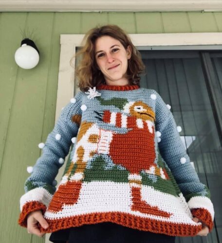 Woman poses wearing a handmade sweater which features an image of the law school mascot, the imaginary creature known as a Peregrinus