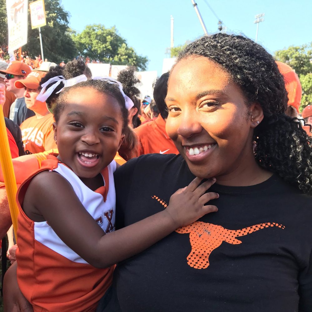 Miatta Echetebu wearing a black shirt with an orange longhorn logo, holding her daughter on her right hip