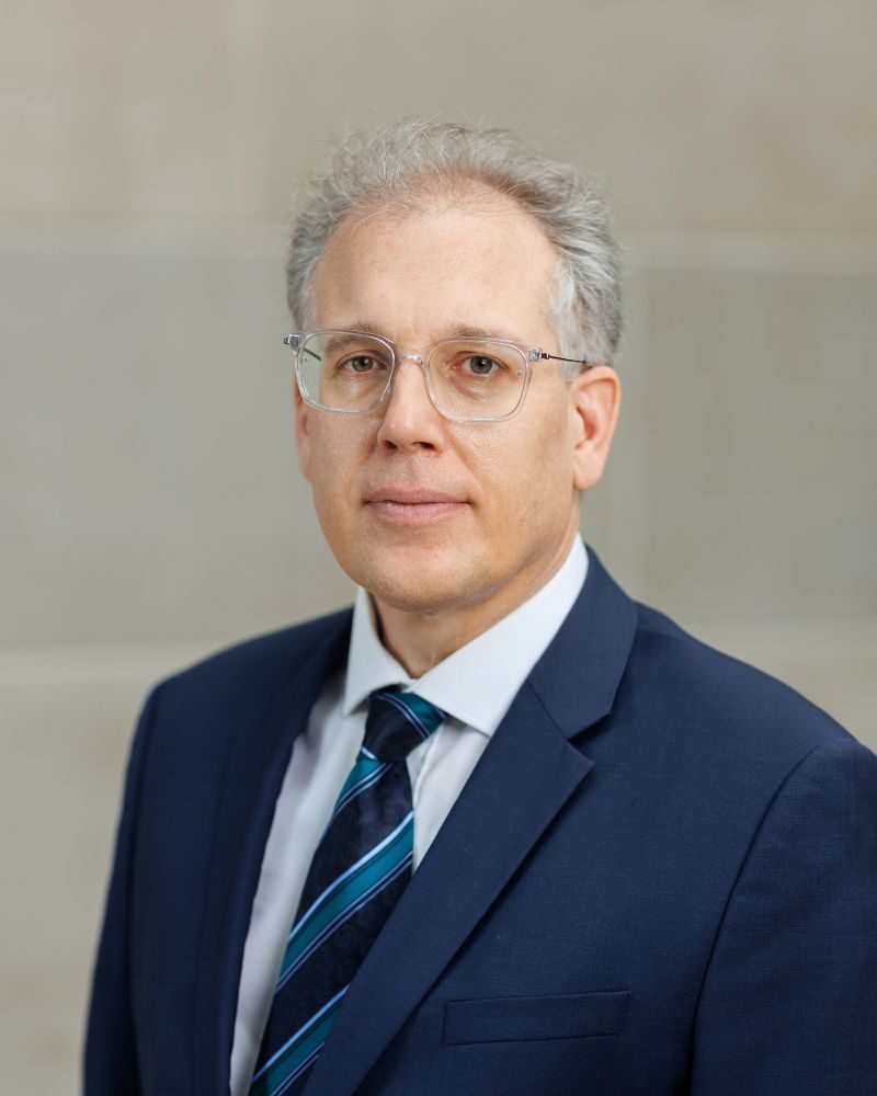 Portrait of Prof. Jens Dammann in glasses wearing a dark blue suit with a blue striped tie