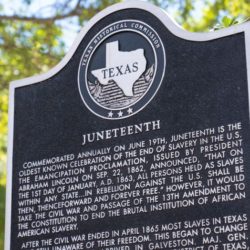 A large metal sign explaining Juneteenth's history in front of trees.