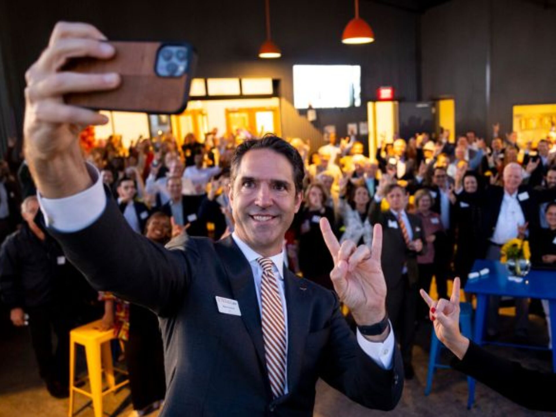 Dean Chesney holding a cell phone to take a selfie with alumni at event
