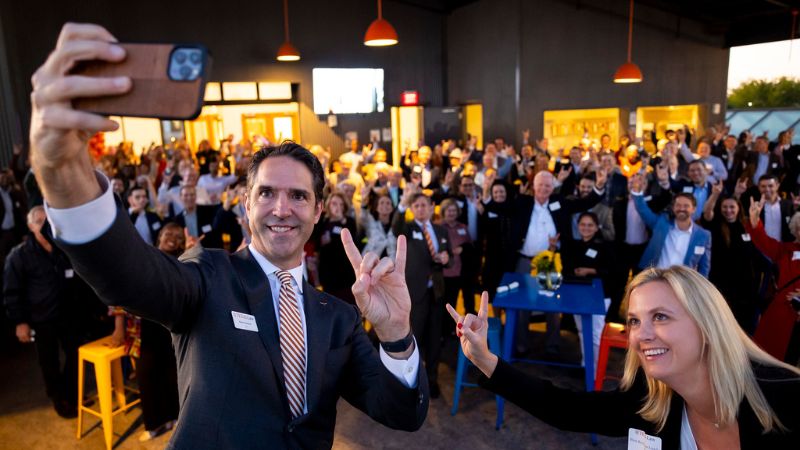 Dean Chesney holding a cell phone to take a selfie with alumni at event