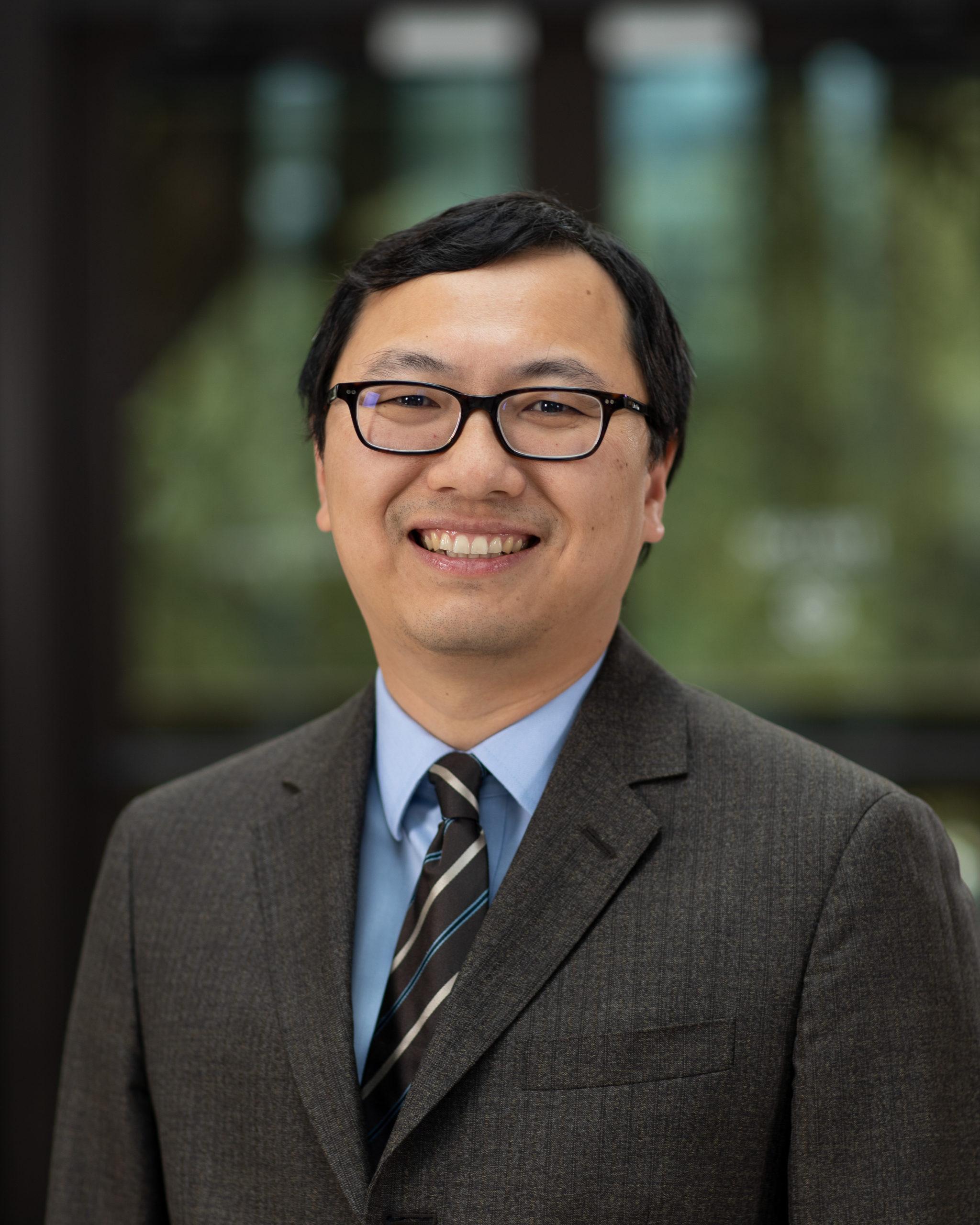 Portrait of Lei Zhang, wearing glasses and a blue shirt with a gray jacket and striped tie.
