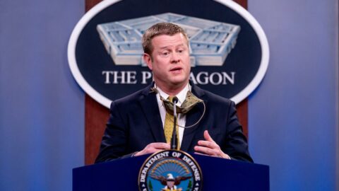 Ryan D. McCarthy wearing a navy jacket and yellow tie, in front of a microphone at the Department of Defense.