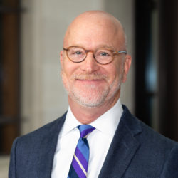 Portrait of The Honorable Robert Pitman, who is wearing glasses and a blue, purple, and white striped tie.