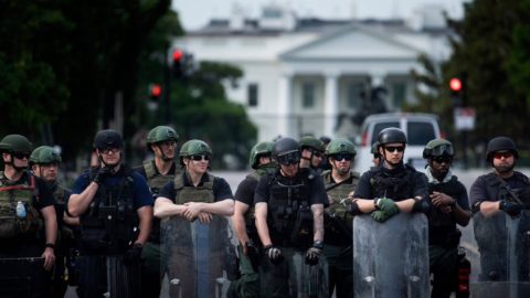 Men in riot gear stand in a line outside the White House