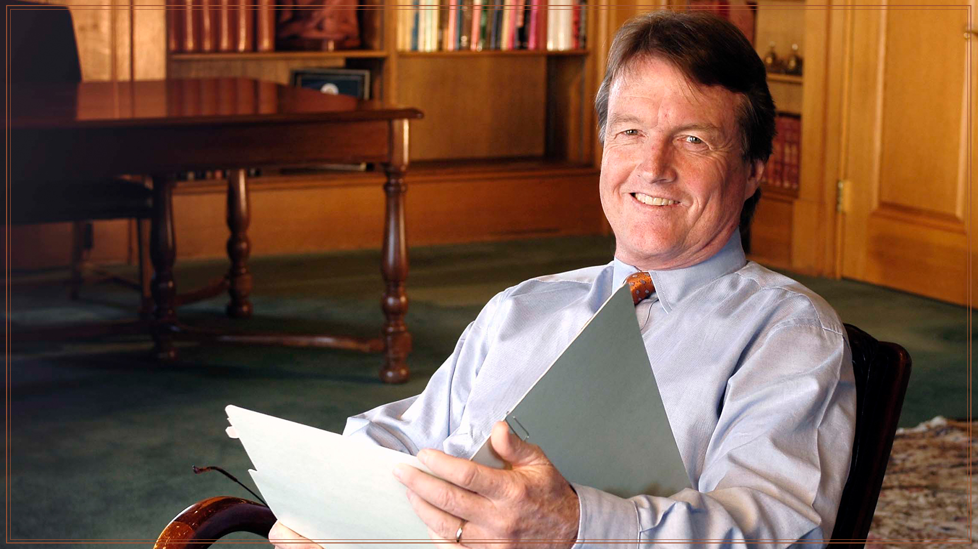 President Bill Powers smiling and opening a file in his office.