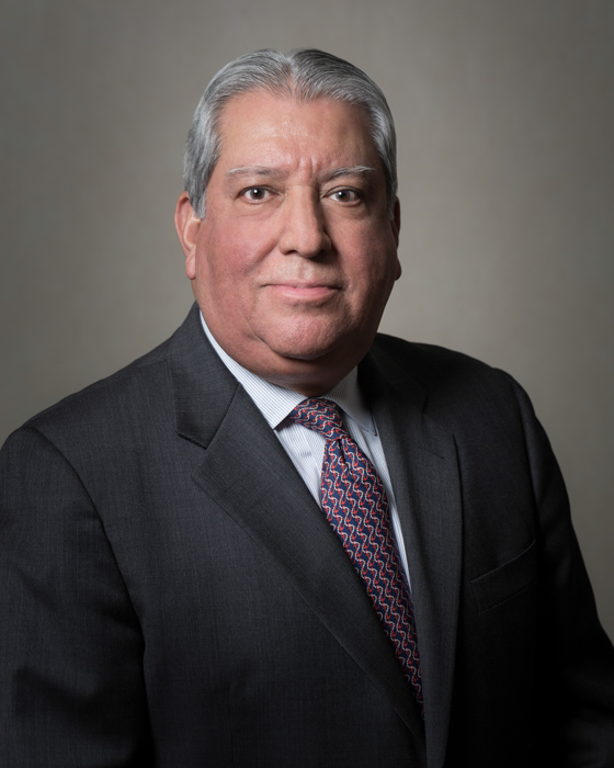 Portrait of Robert Estrada, wearing a black jacket and a red and black tie.