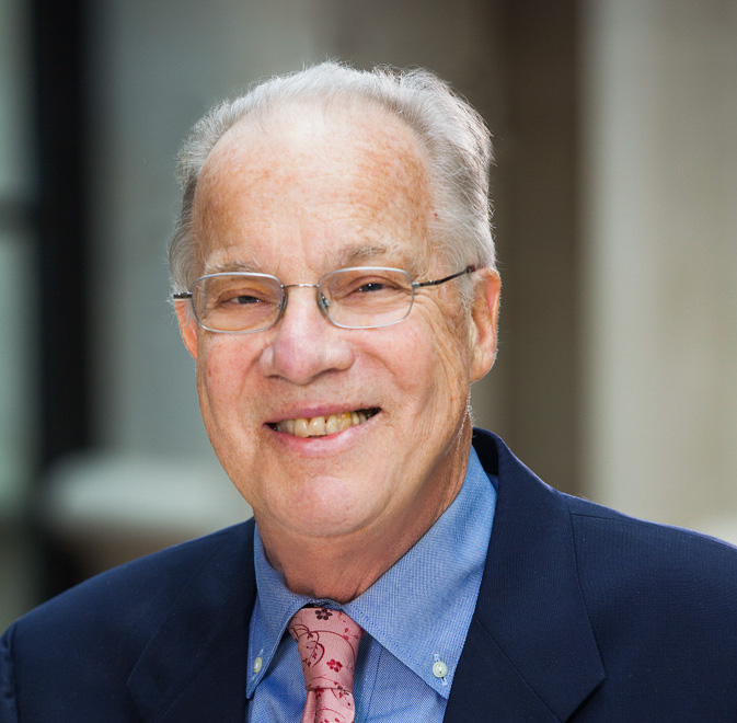 Portrait of Prof. John A. Robertson, wearing glasses, a blue shirt and jacket with a peach tie.