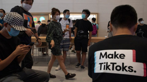 Young people in COVID masks use cell phones; a t-shirt in the foreground reads "Make TikToks"
