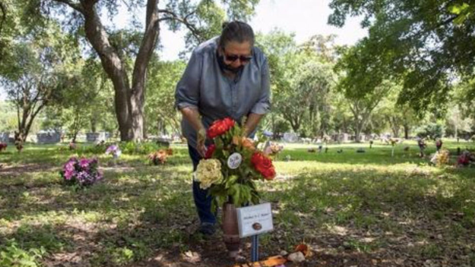 A women wearing a COVID face mask stands over flowers marking a grave in a cemetery
