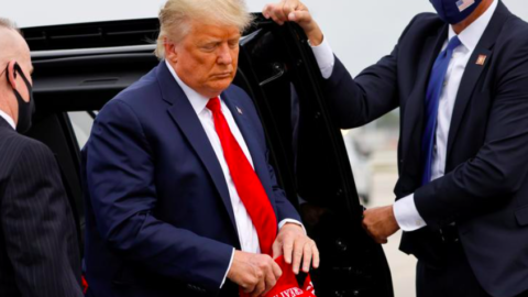 President Trump holding a red Make America Great Again hat, stepping out of a black car.