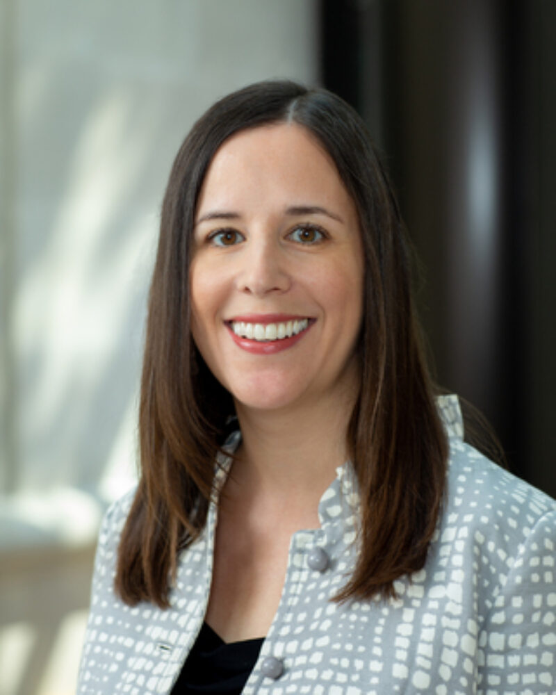 Portrait of Prof. Elizabeth Sepper wearing a black shirt underneath a grey and white jacket.