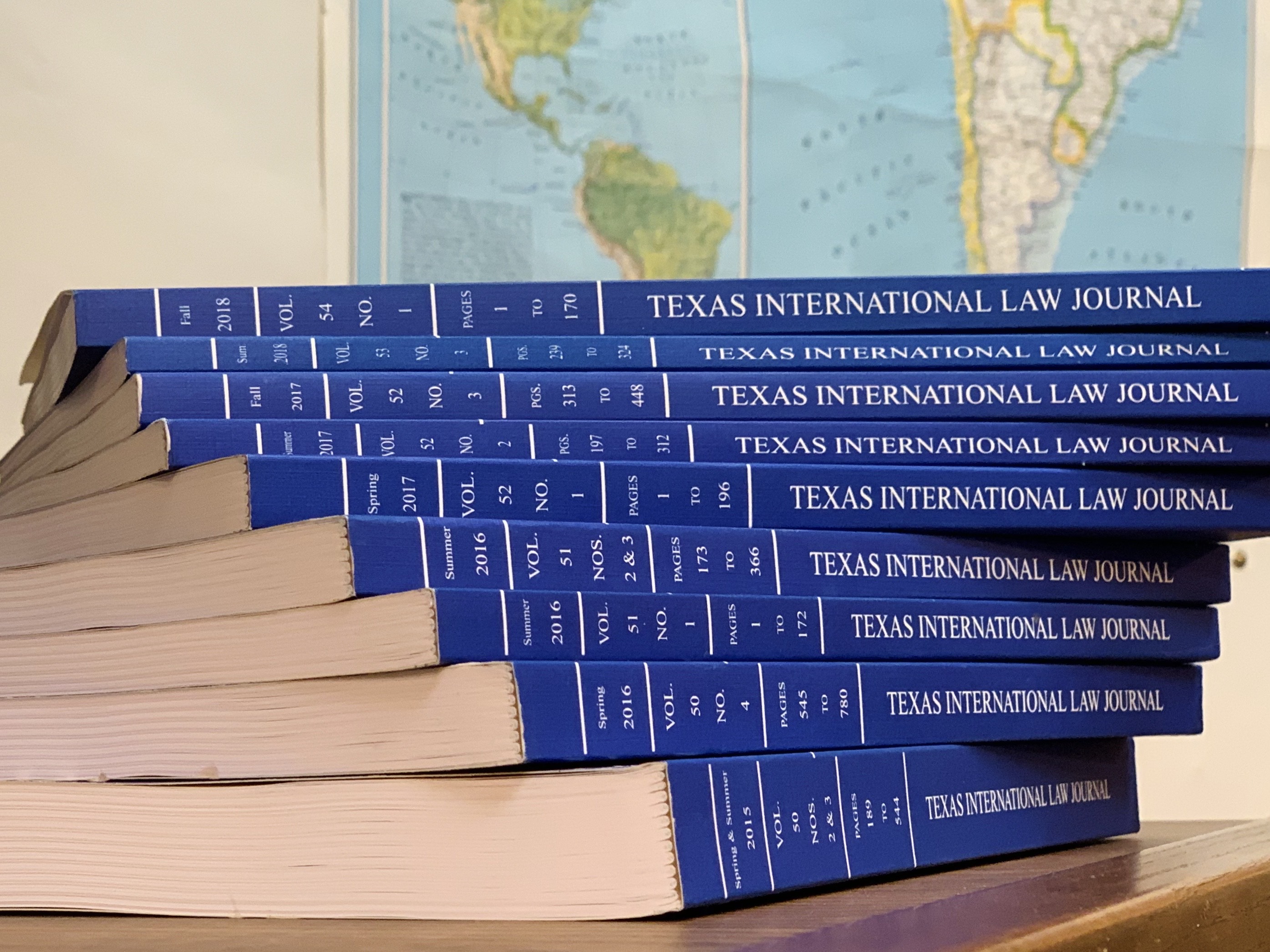 A stack of the blue Texas International Law Journal books, with a world map hanging on the wall behind them