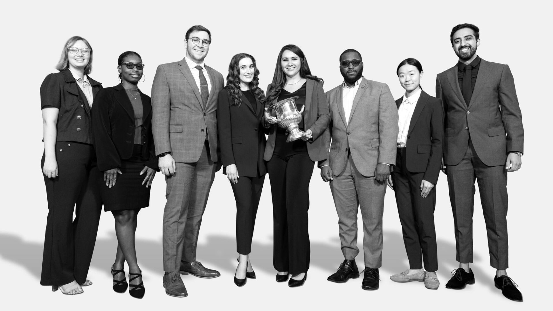 Black and white photo of group of students in business suits holding a trophy