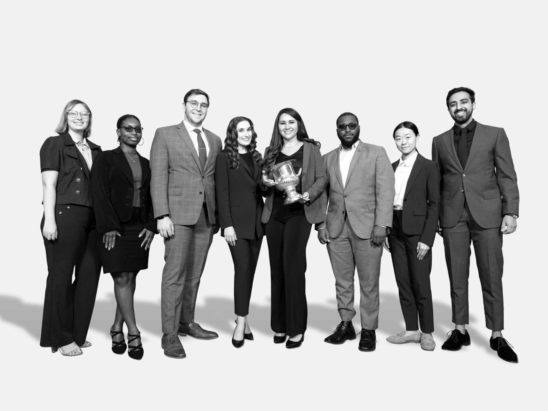 black and white photo of group of students in business suits holding a trophy