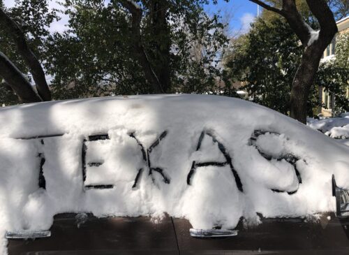 A car covered in snow with the word "Texas" drawn in the snow, taken during Winter Storm Uri in February 2021