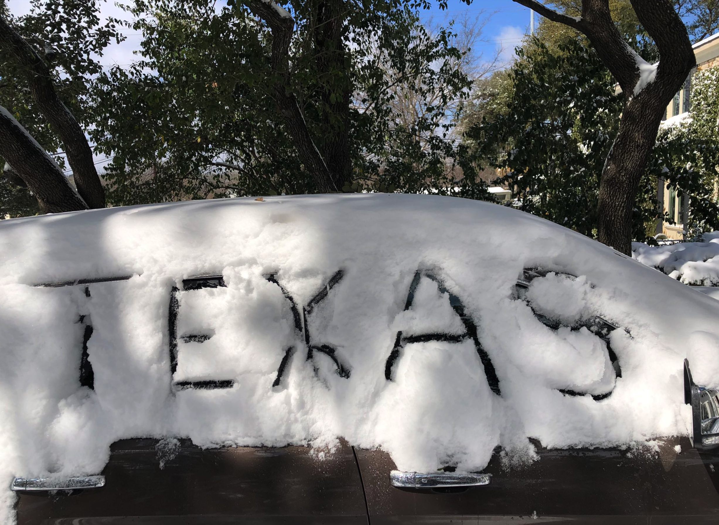 A car covered in snow with the word "Texas" drawn in the snow, taken during Winter Storm Uri in February 2021