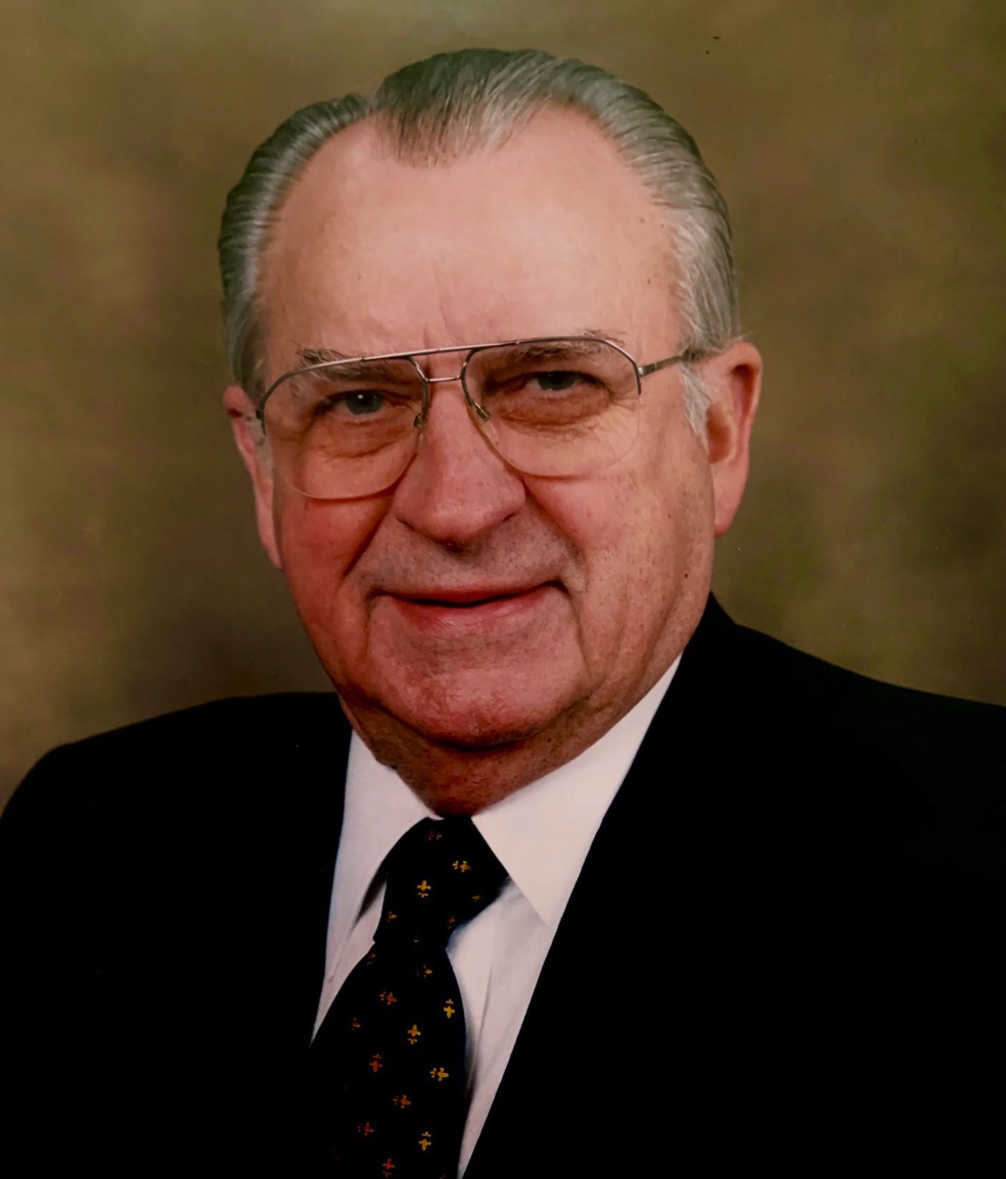Portrait of Thomas M. Reavley, wearing glasses and a suit with a black jacket and black and gold tie.